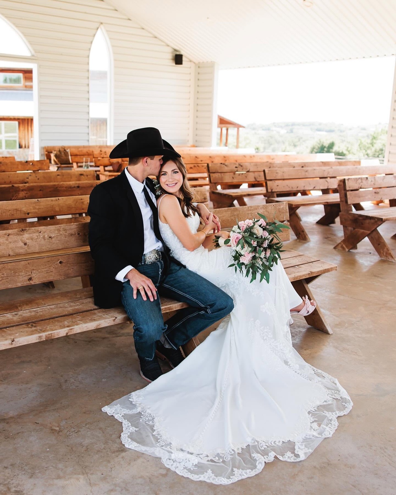 A bride and groom seated on a wooden pew inside the open-air chapel at Diamond H3 Ranch, hill-country views beyond